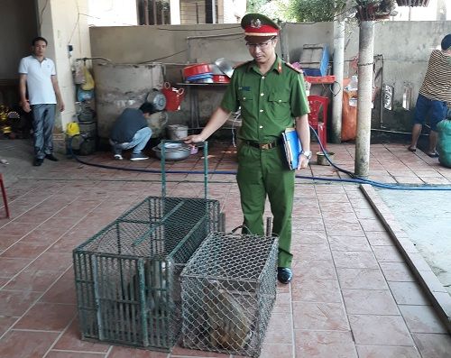 A person in a uniform standing next to a cage with animals
Description automatically generated
