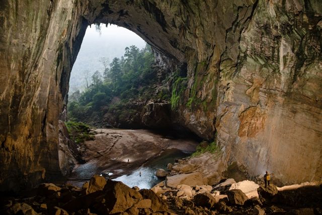 A cave with a river and trees Description automatically generated