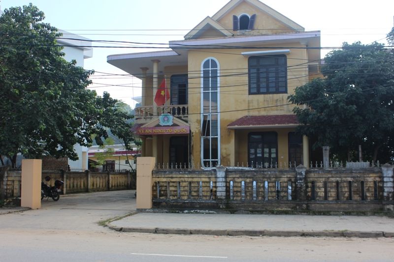 A yellow house with a fence and trees Description automatically generated